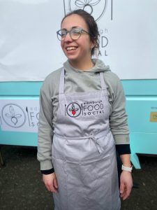 Photograph of a woman wearing a grey embroidered Edinburgh Food Social apron
